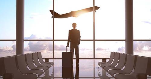 Business man standing with suitcase in front of airport window, watching a plane take off