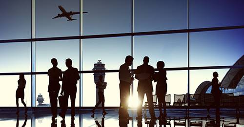 Silhouettes of people standing in an airport, with the sun shining through the window